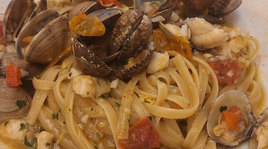 Linguine con vongole, bocconcini di pesce bianco, pomodorini rossi e gialli e prezzemolo tritato in un piatto bianco